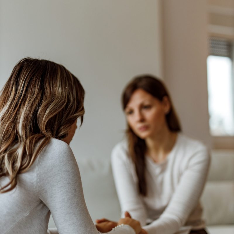 Focus on depressed woman, brunette doctor in the background.