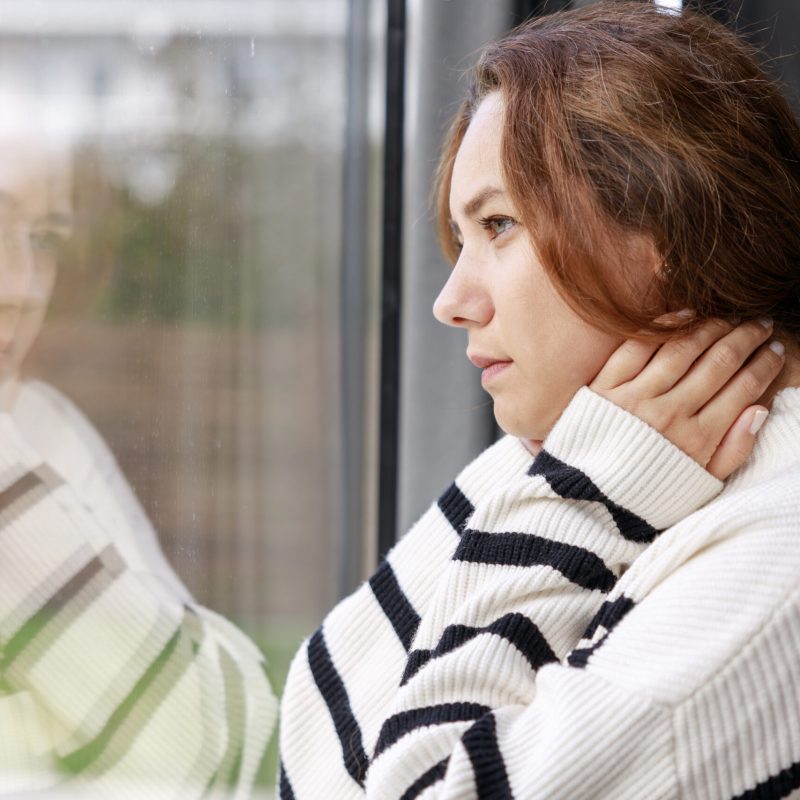 Worried woman standing near window alone at home. Concept of end of relationship and unsuccessful emotion